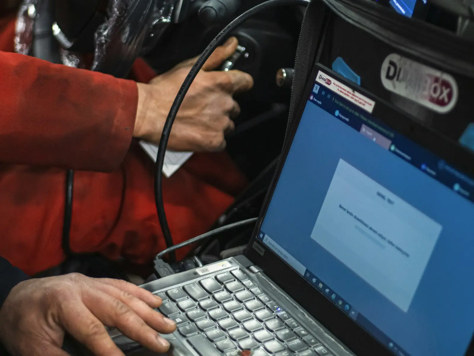 A mechanic plugs a scan tool into a car and reads the results on a laptop