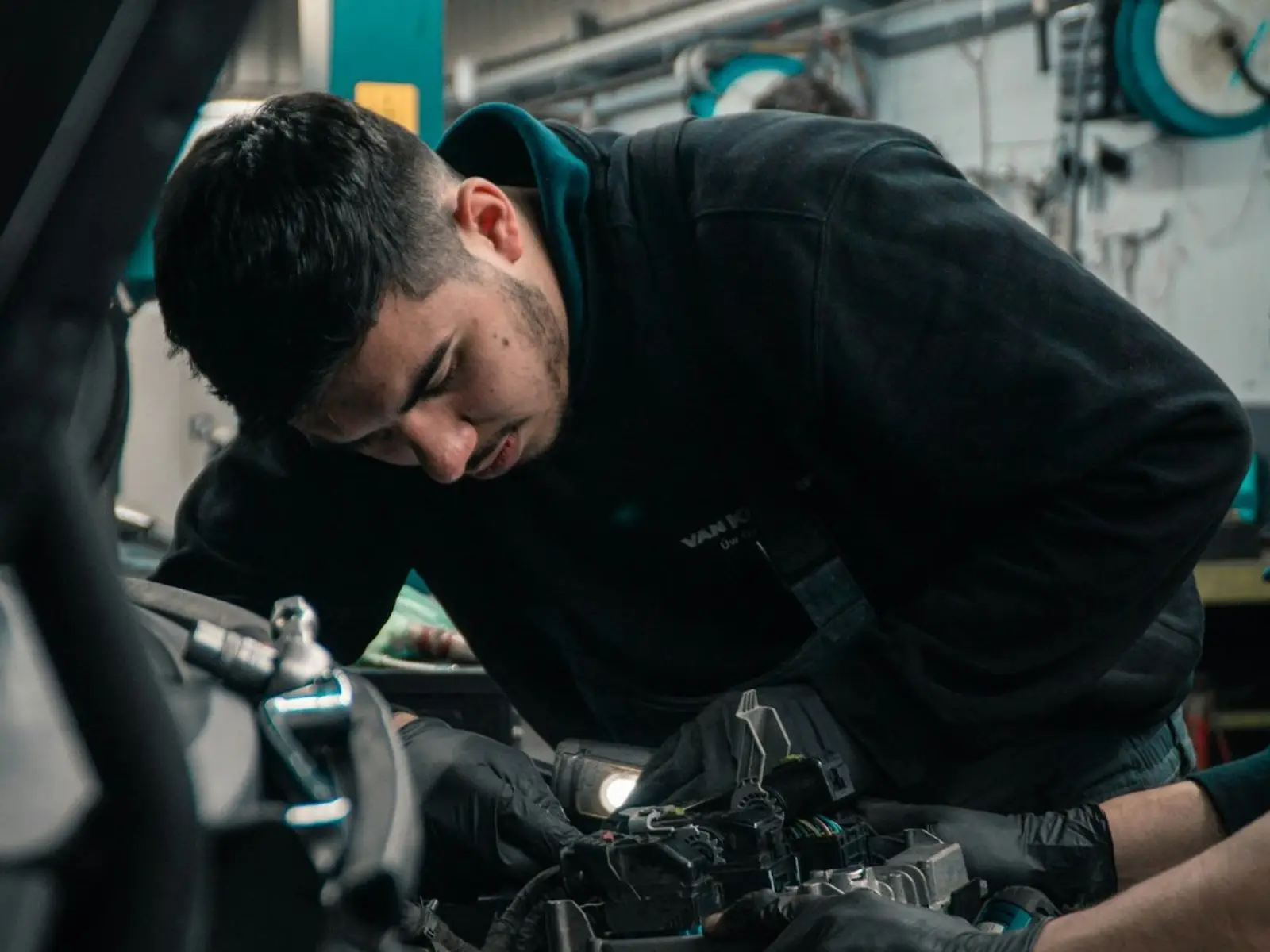 A mechanic in gloves works on wiring under the hood