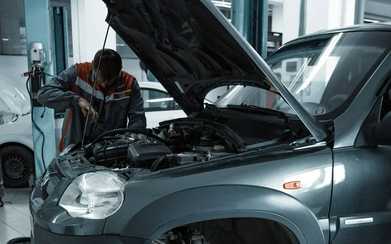A mechanic leans into the engine bay of an SUV with its hood up, in a bright repair shop